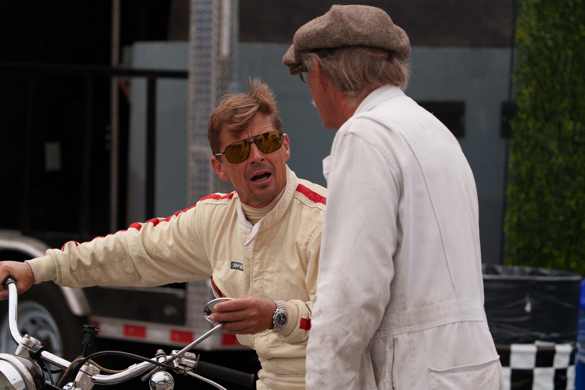 Two drivers in vintage racing suits talking in the paddock