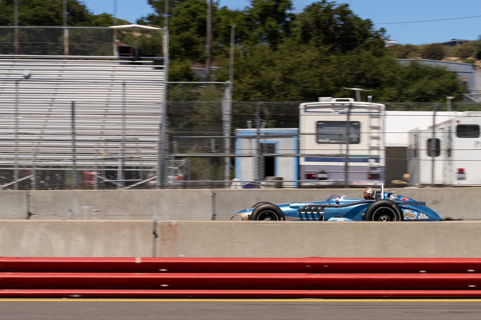 Blue vintage open-wheel race car speeding past on track