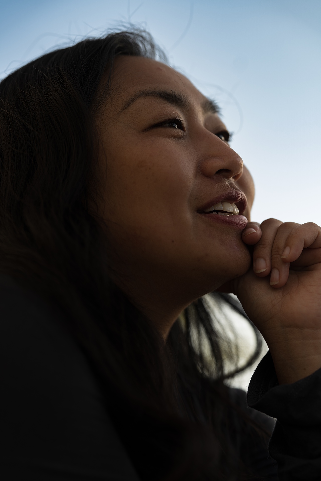 Woman gazing upward with chin resting on hand, backlit against open sky