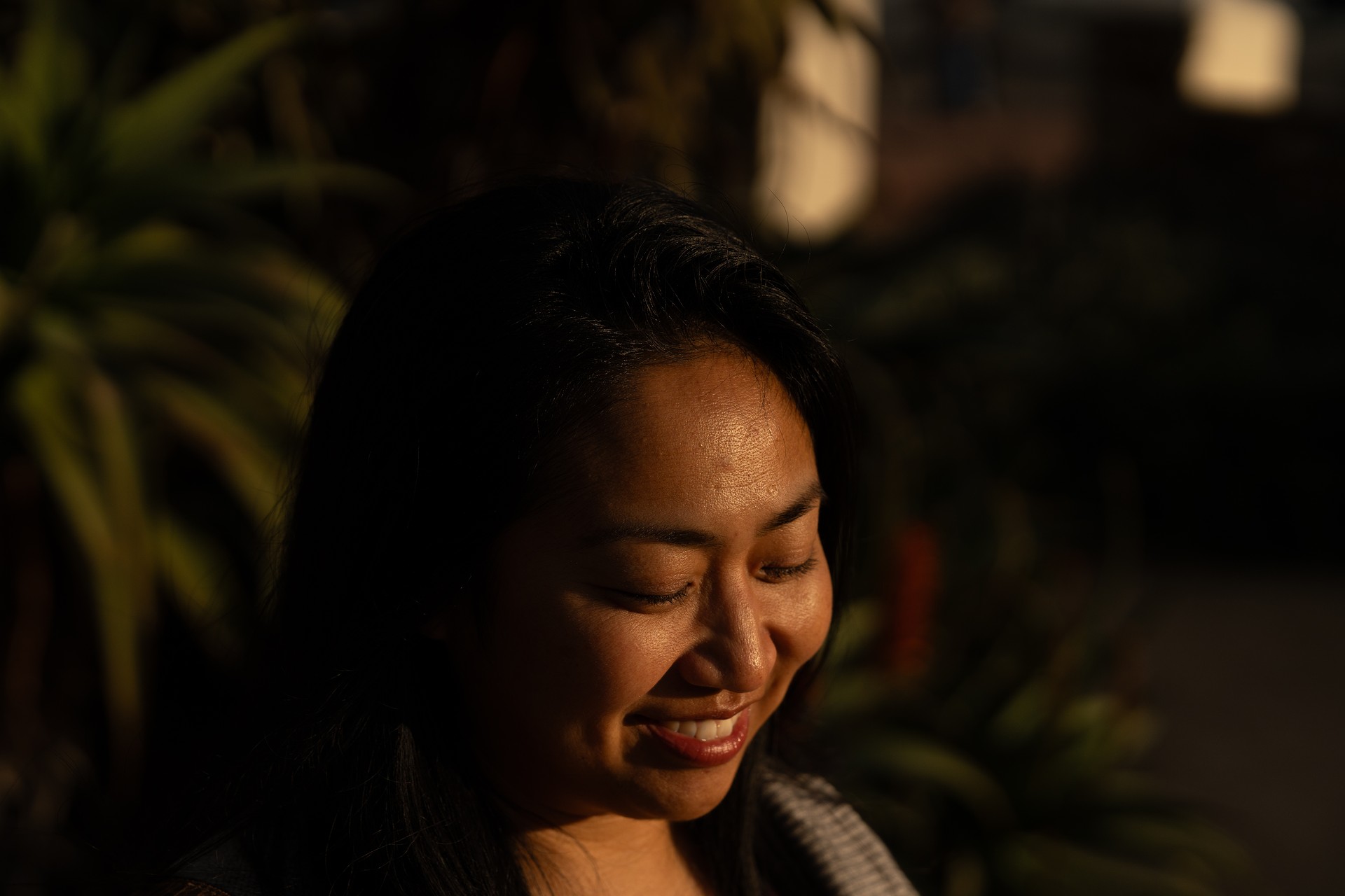 Woman smiling with eyes closed in warm golden hour light, plants behind